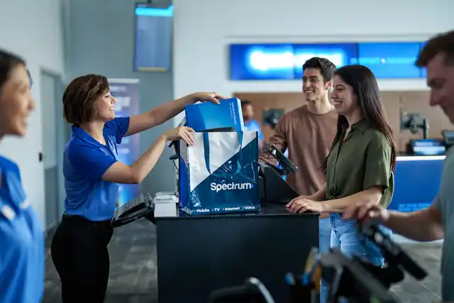 Store associate handing a customer a Spectrum router bag at the counter